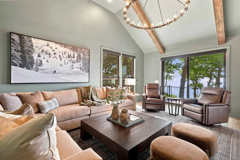Great room with exposed beams, an iron ring chandelier and a camel sectional facing a wall of windows
